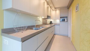 A modern kitchen with white cabinets, a stainless steel sink, and a microwave. - Calista 213 with balcony by Interhome (Bredene)