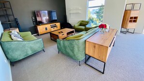 Een moderne woonkamer met een bank, salontafel en televisie. Een raam biedt uitzicht op bomen en bergen.