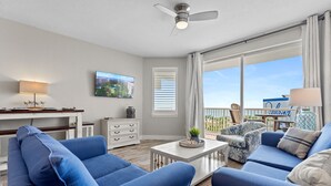 A modern living room with blue sofas, a white coffee table, a ceiling fan, and a large window with blinds. - Destin West Gulfside 510 ~ Amazing Beach Views ~ Beach Service (Fort Walton Beach)