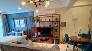 A modern hotel room with a bed, sofa, TV, bookshelf, and dining area. - Deluxe Studio at Timurbay with Seaview (Kuantan)