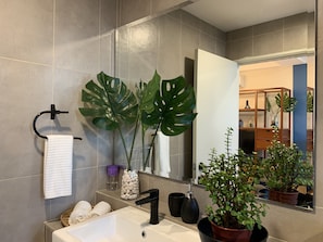 A modern bathroom with a white sink, black faucet, and large mirrors. There are two large green plants and a potted plant on the counter. - Deluxe Studio at Timurbay with Seaview (Kuantan)