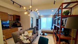 A modern living room with a sofa, a dining table, and a bookshelf. There is a kitchen area with a washing machine and a dining table. - Deluxe Studio at Timurbay with Seaview (Kuantan)