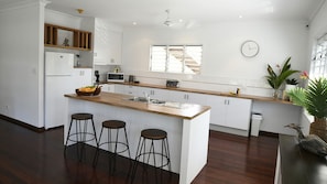 Une cuisine moderne avec un îlot central, des tabourets de bar, des meubles blancs et une horloge au mur.