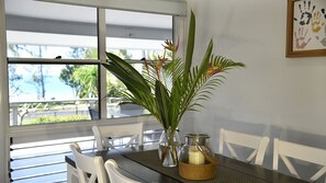 A dining area with a table set for two, a vase with flowers, and a candle holder. - Ohana - Beachfront Holiday House (South Mission Beach)