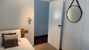 Un dormitorio con cama, mesita de noche, espejo en la pared y puerta que da a otra habitación.