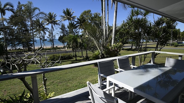 Une terrasse avec une table et des chaises donnant sur une plage bordée de palmiers.