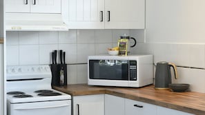 Une cuisine avec des armoires blanches, une cuisinière blanche, un four à micro-ondes et une machine à café posée sur le plan de travail.