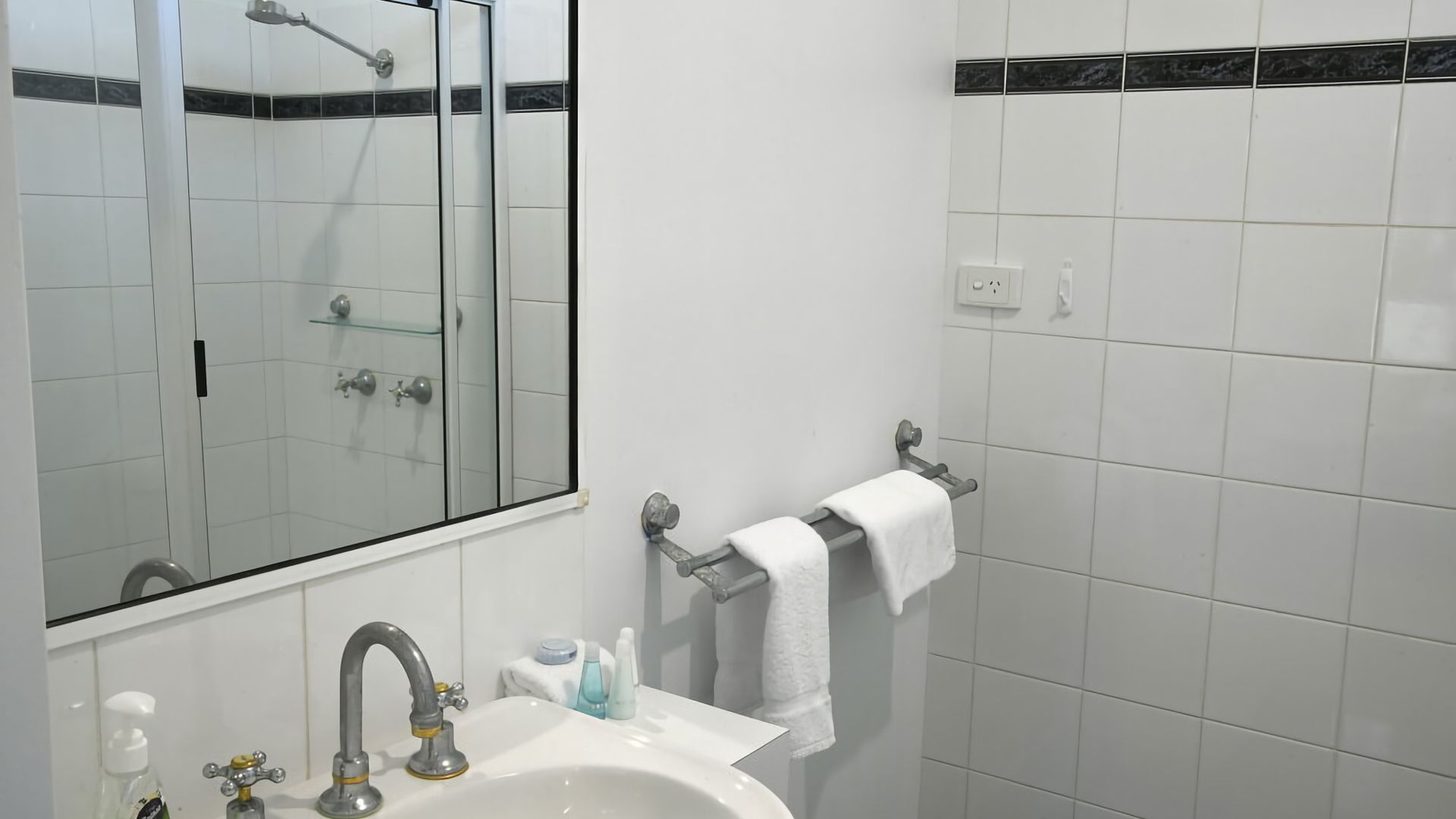 A bathroom with a white sink, a mirror, a towel rack, and a shower area.