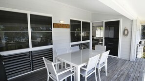 A covered patio with a table and chairs, large windows, and a view of the outdoors.