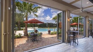 A glass-enclosed patio with a pool view, outdoor seating, and palm trees.