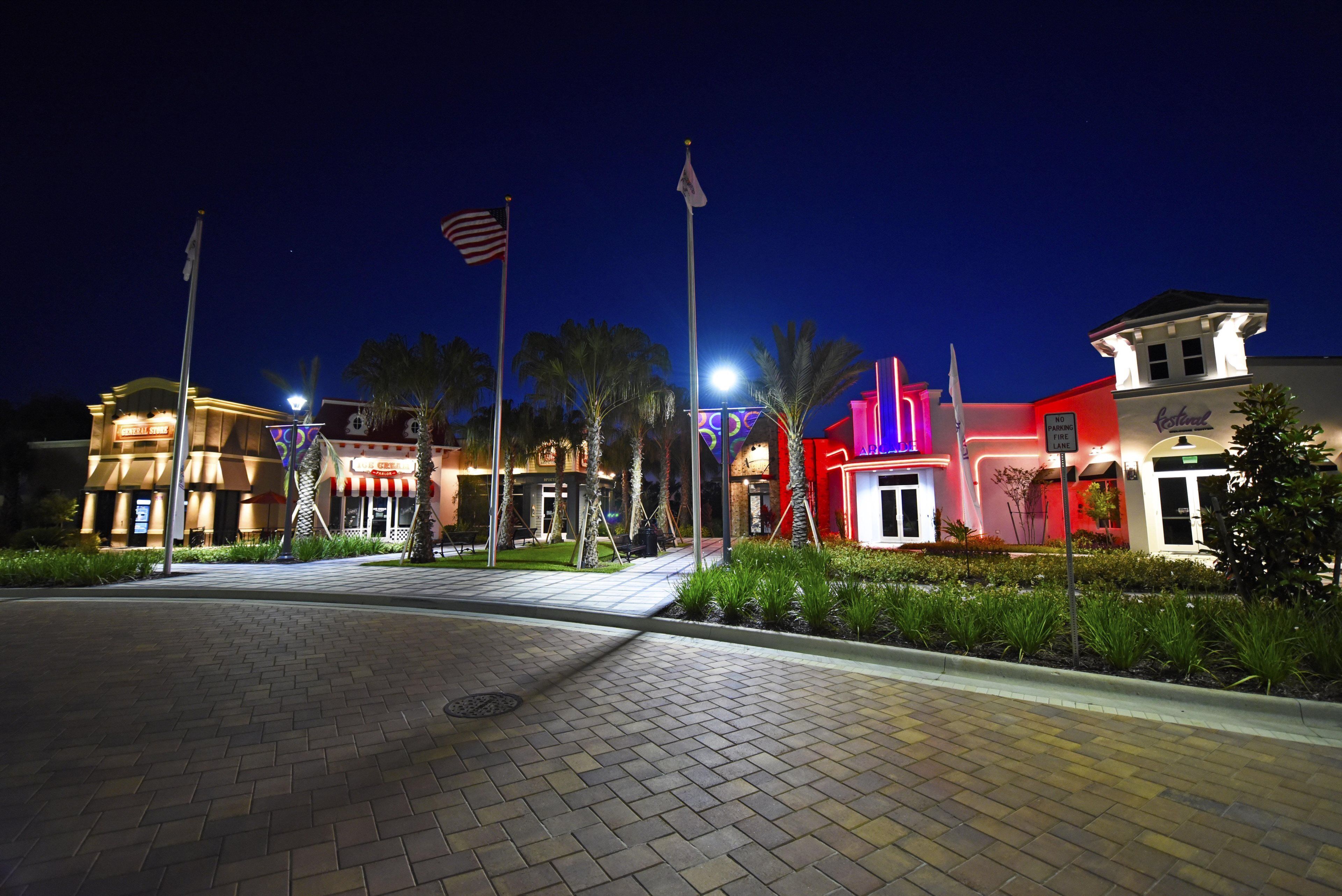 A nighttime view of a hotel with a paved walkway, palm trees, and illuminated buildings.