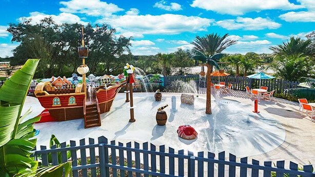 A water park with a pirate ship, water slides, and a fenced area with chairs.
