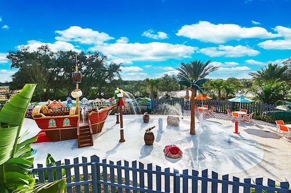 A water park with a pirate ship, water slides, and a fenced area with chairs.
