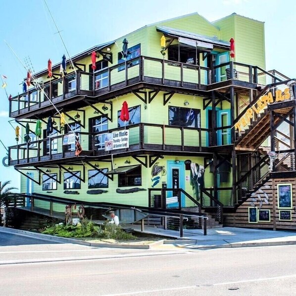 Un edificio de varios pisos con balcones, un cartel anunciando música en vivo los jueves y domingos, y una escalera a la derecha.