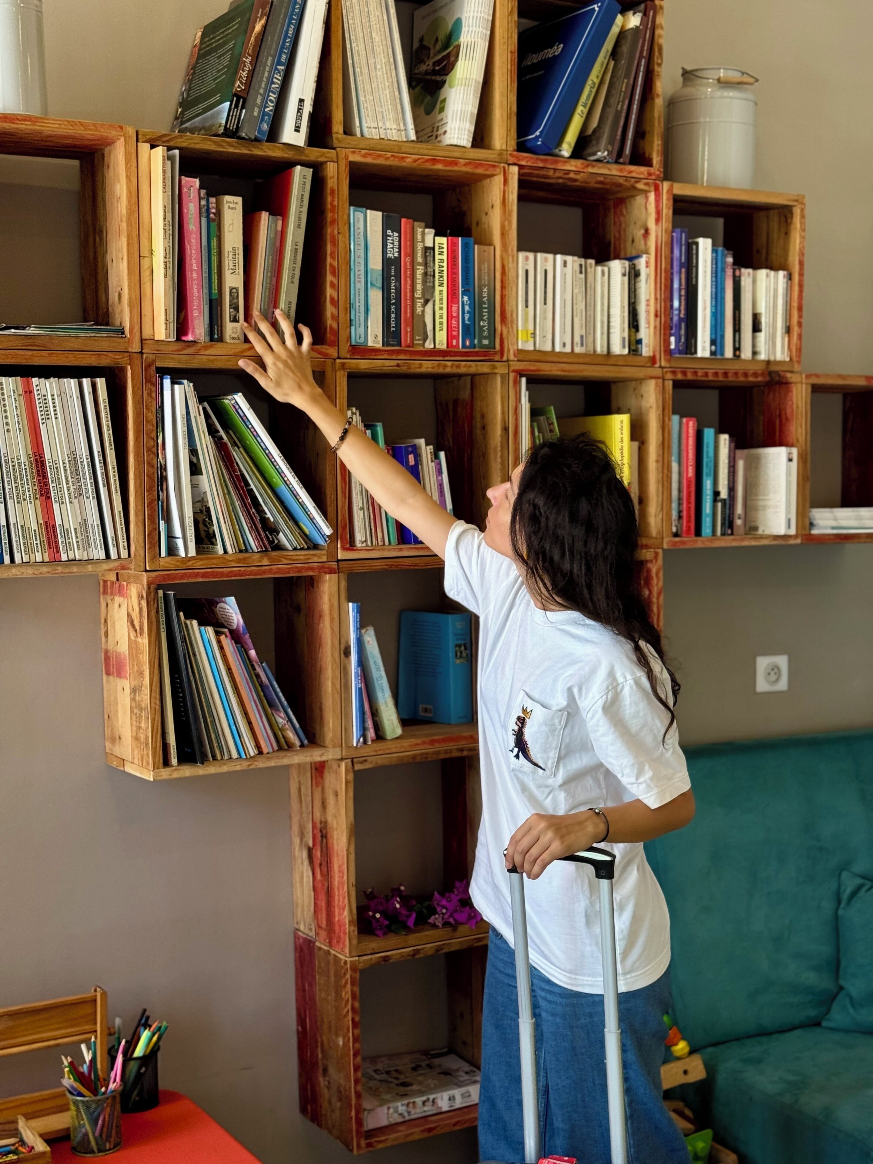A person reaching for a book on a wooden bookshelf.