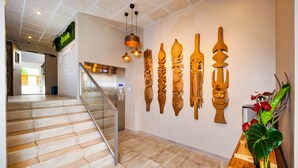 A hotel lobby with a staircase, a reception desk, and a wall decorated with wooden carvings. - Hôtel Gondwana - City ART (Nouméa)
