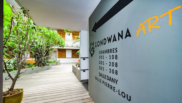 A hotel corridor with a sign listing room numbers and names. - Hôtel Gondwana - City ART (Nouméa)