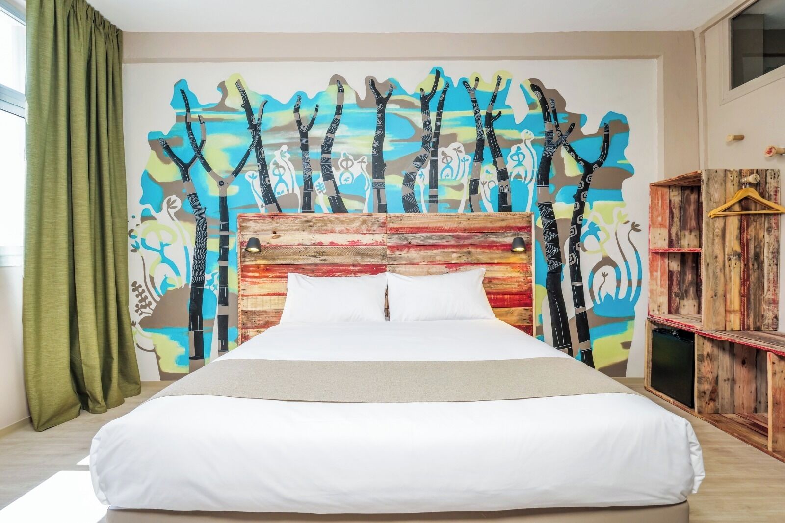 Una cama con cabecera de madera, un mural abstracto de colores en la pared y un mueble de madera con un televisor.