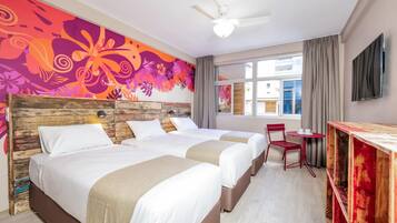 Habitación de hotel con dos camas, cabecera de madera, una silla roja, una mesita y un televisor en la pared.