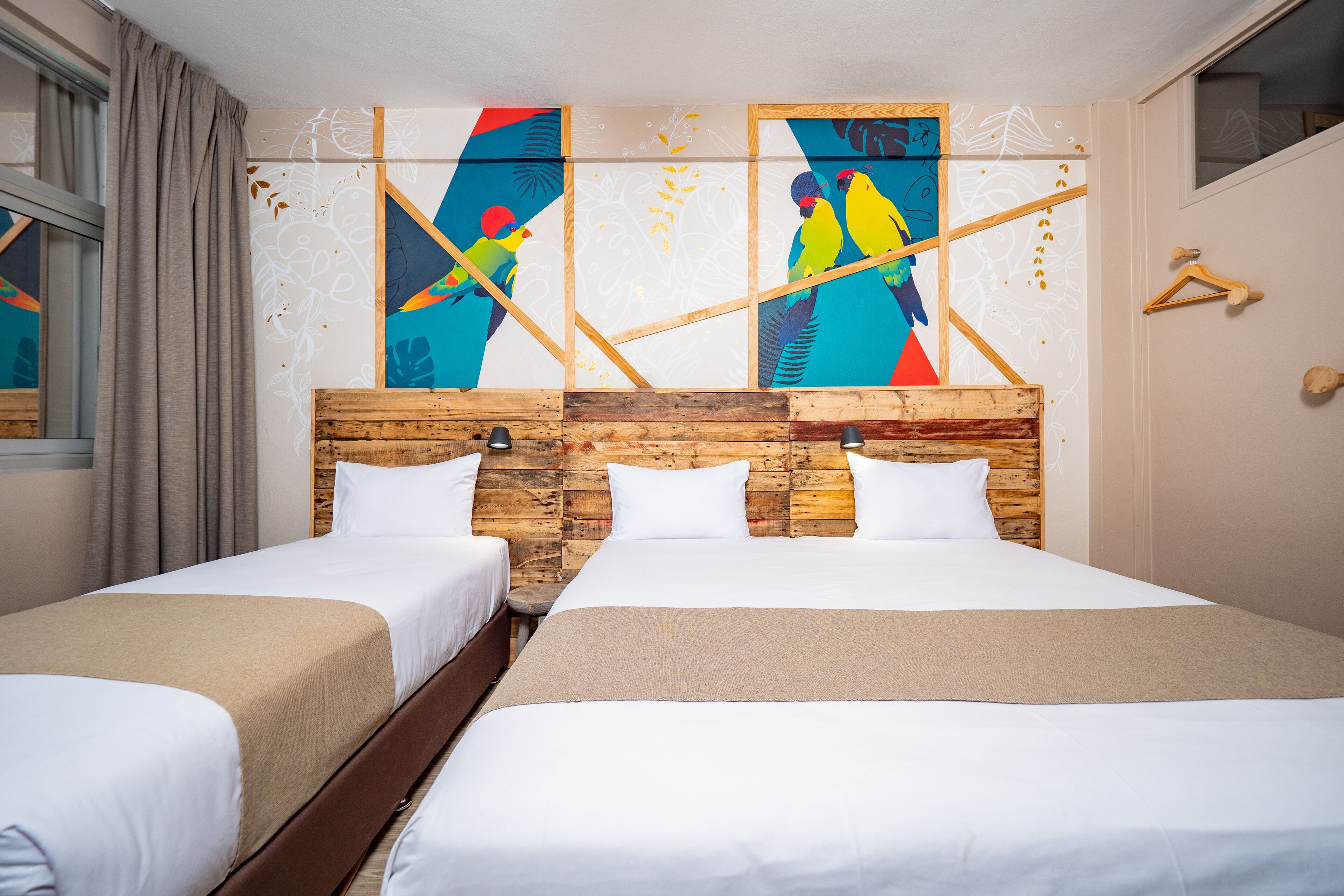 Une chambre double avec deux lits, une tête de lit en bois, du linge de lit blanc et des œuvres d'art colorées accrochées au mur.