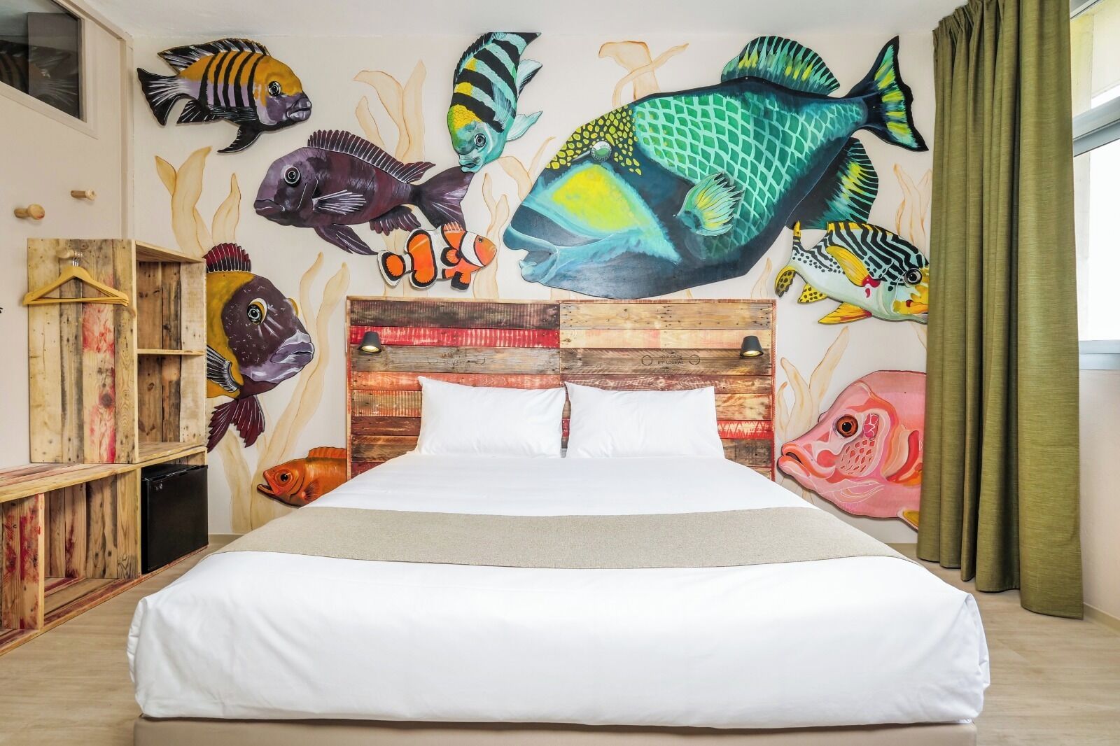 A bedroom with a bed, wooden headboard, and a wall mural of colorful fish.
