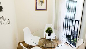 Una piccola zona pranzo con tavolo in vetro e sedie bianche, una pianta in vaso e un quadro appeso alla parete.