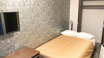 A hotel room with a bed, a desk, a television, and a door.