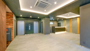 Un lobby amplio con diseño moderno, que incluye una recepción, ascensores e iluminación empotrada en el techo.