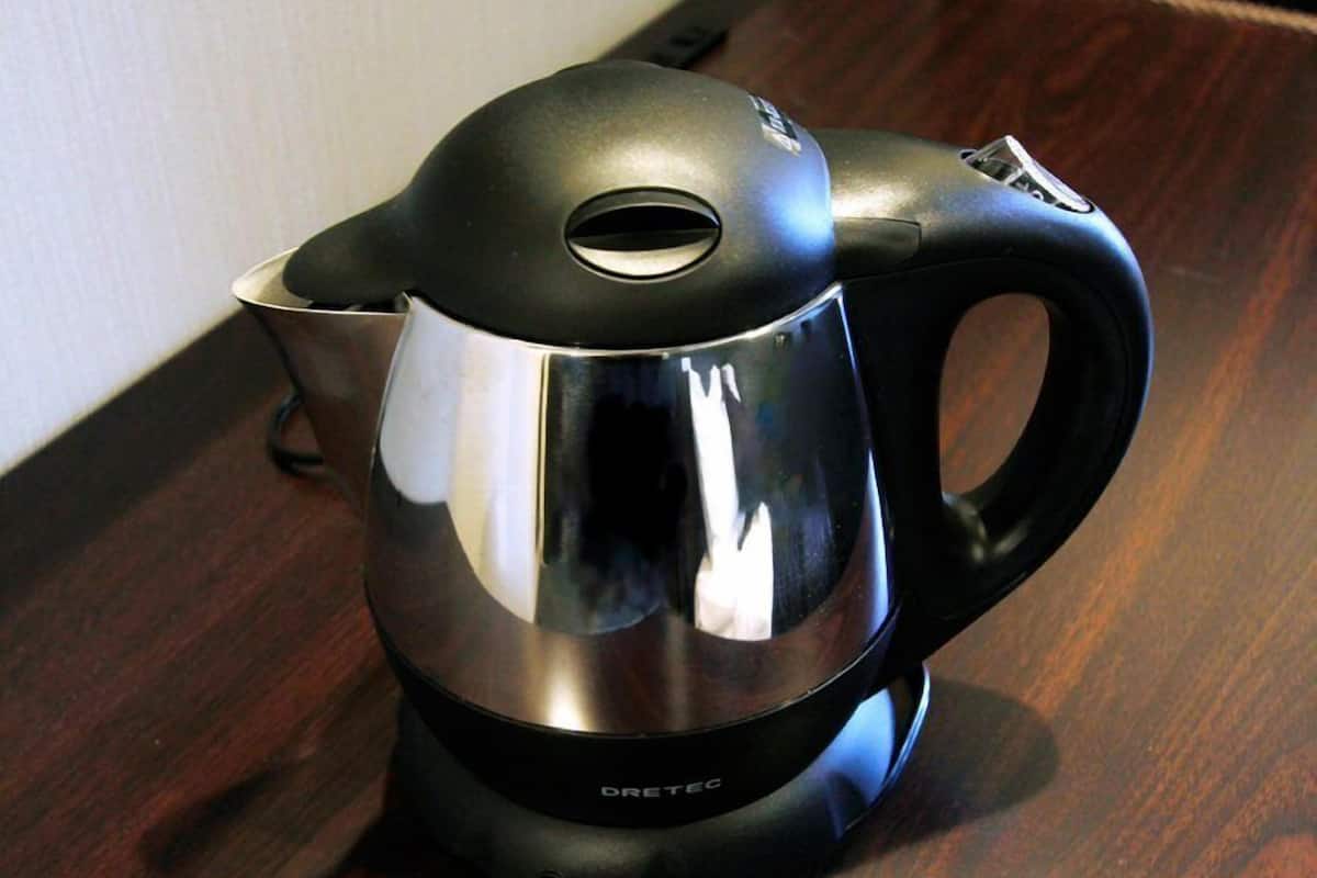 A stainless steel electric kettle with a black handle and base, placed on a wooden surface.