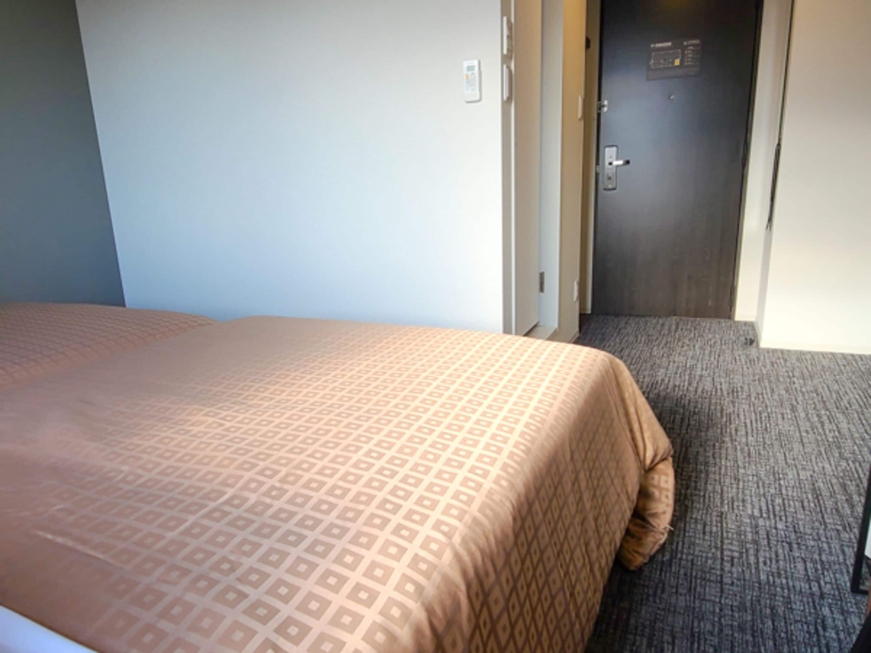 A hotel room with a bed, a door, and a carpeted floor.
