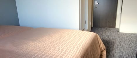 A hotel room with a bed, a door, and a carpeted floor.