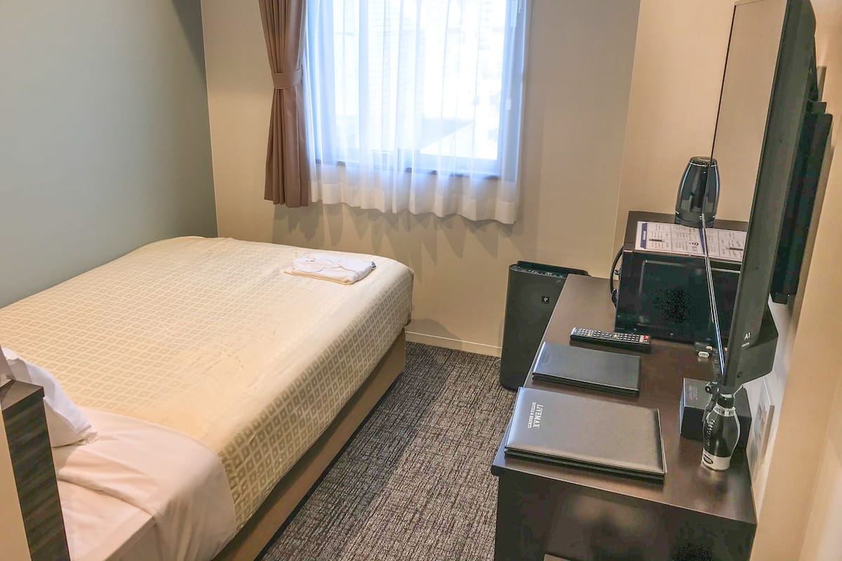 Een hotelkamer met een bed, een bureau met een computer, een spiegel en een raam met gordijnen.