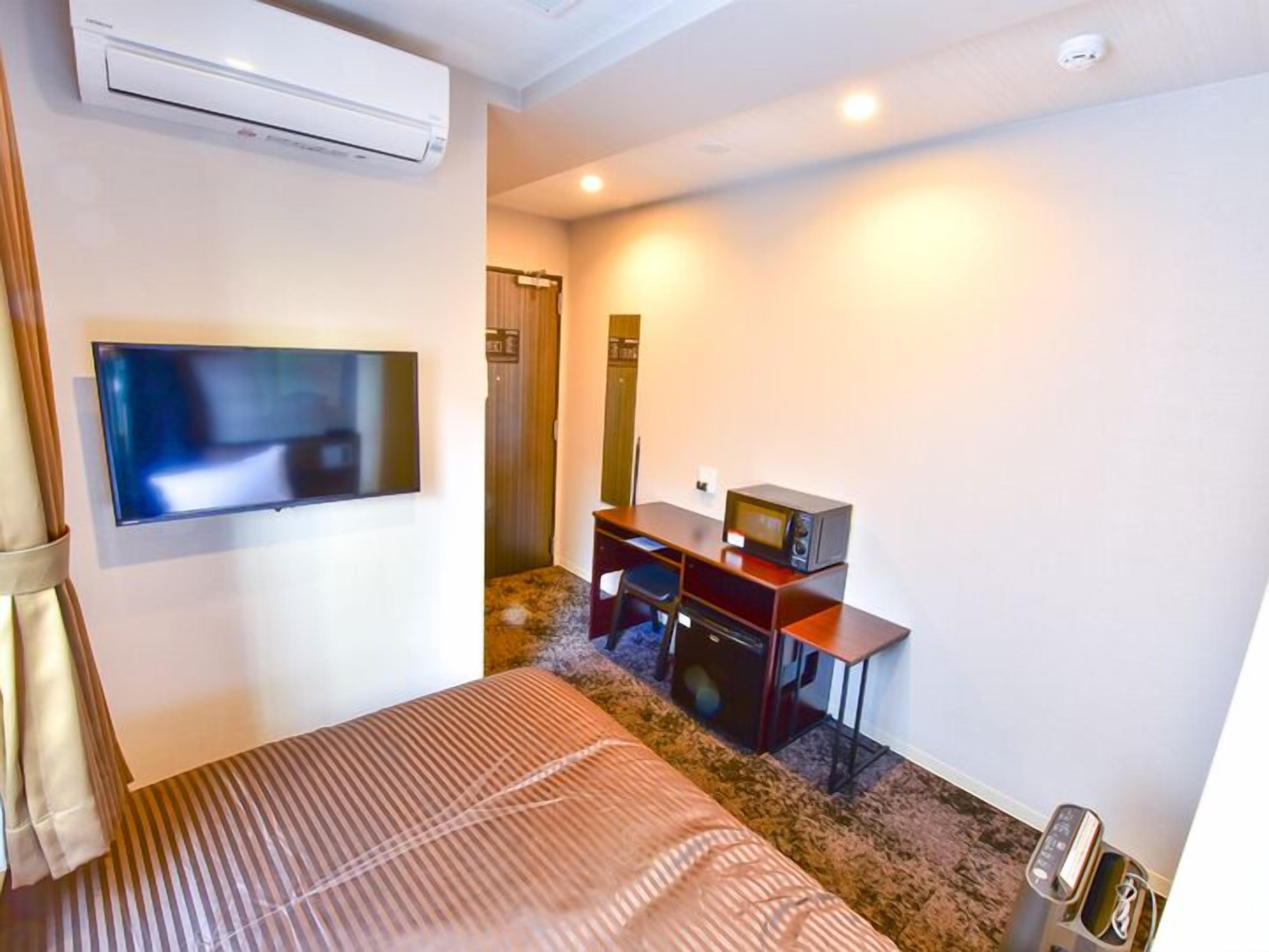 Habitación de hotel con cama, televisor de pantalla plana, escritorio con computadora, microondas y aire acondicionado.