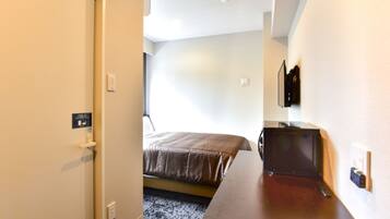 A hotel room with a bed, a desk, and a television mounted on the wall.