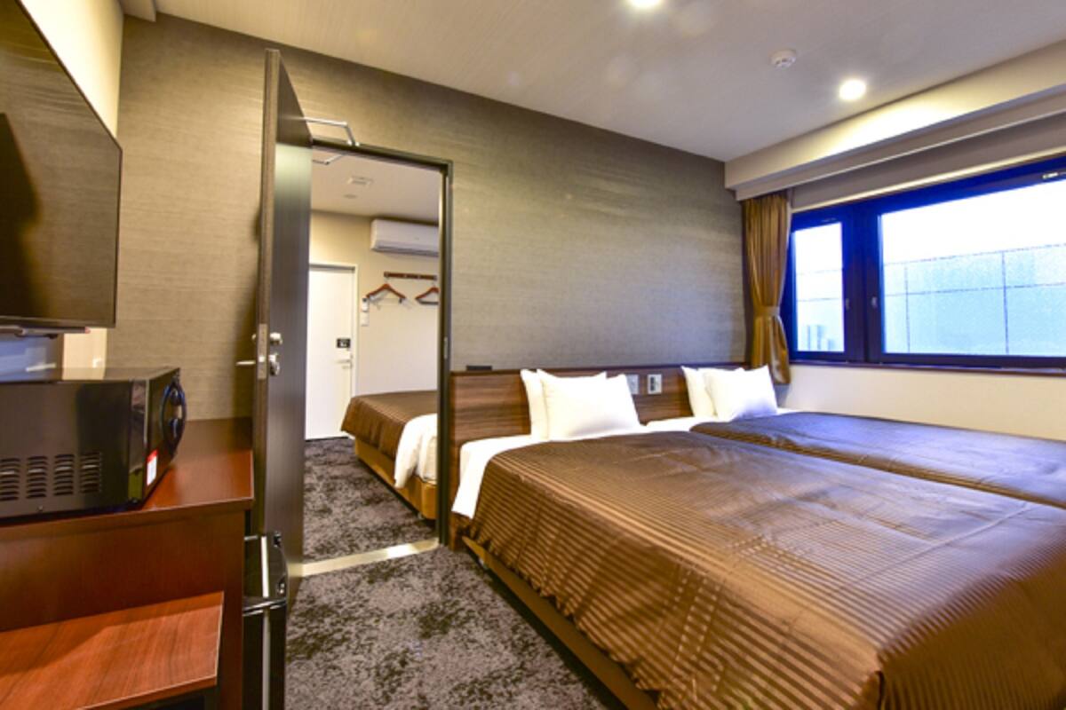 A hotel room with a bed, a desk, a TV, and a window with curtains.