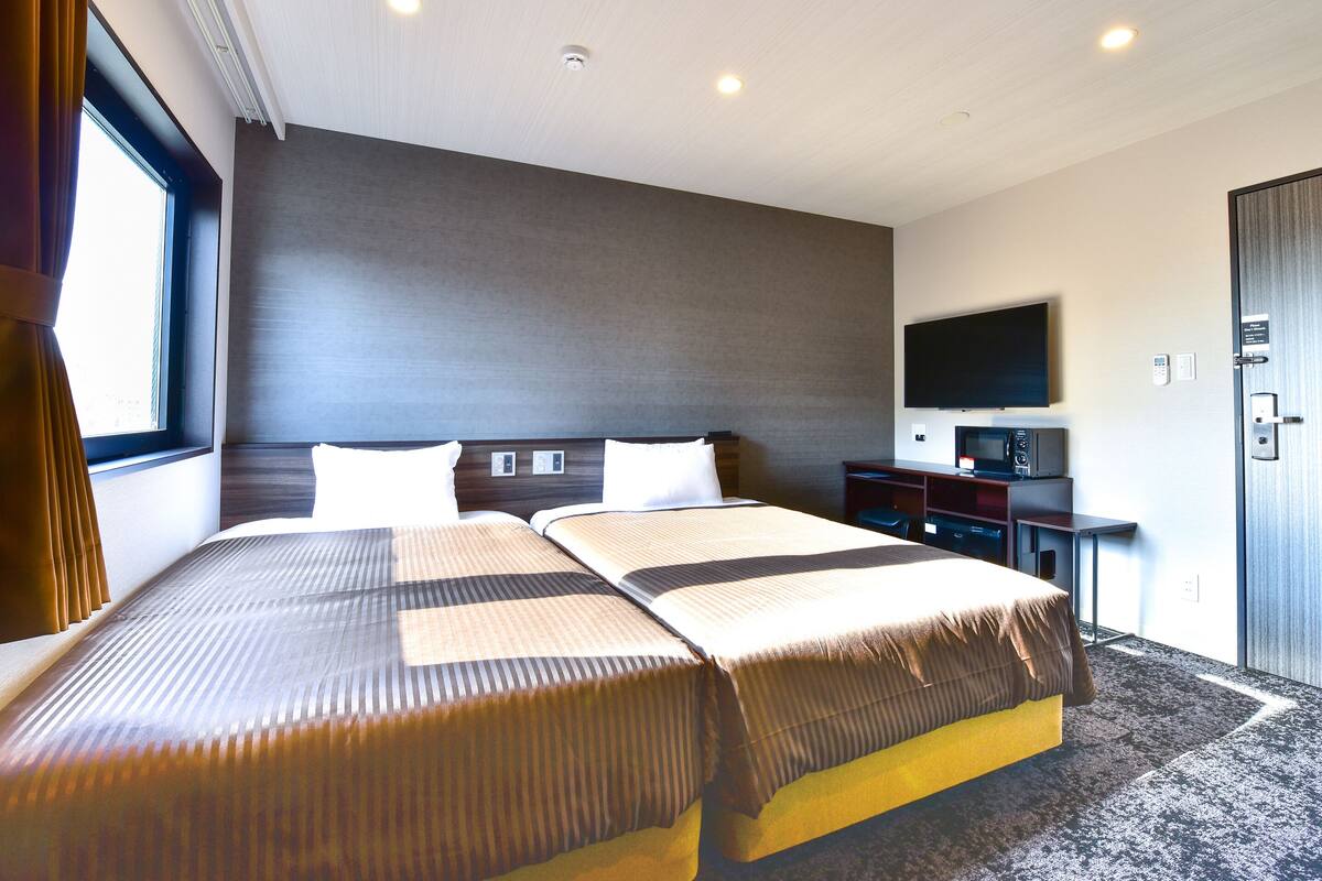 A hotel room with two beds, a flat-screen TV, a desk, and a wardrobe.