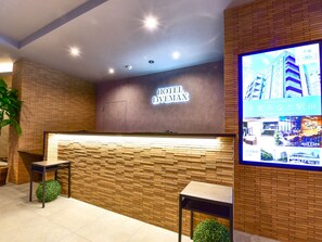 Un espace d’accueil d’hôtel au design moderne, comprenant un comptoir d’accueil, un panneau mural et un écran numérique.