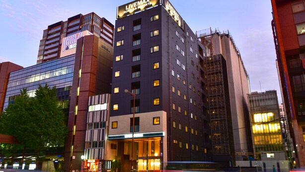 Un hôtel moderne, reconnaissable à son grand panneau lumineux « LIVEMAX », avec de nombreux étages et une entrée bien éclairée.