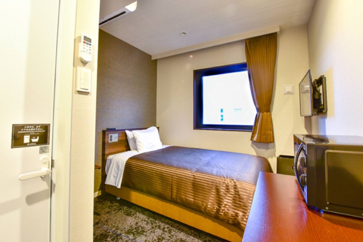 A hotel room with a bed, a desk, a television, and a window with curtains.