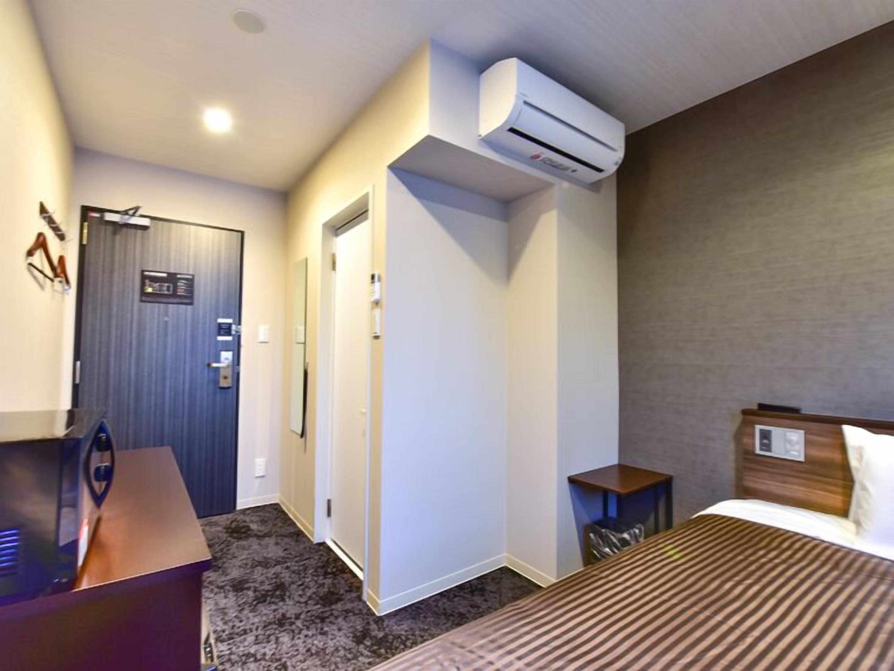 Una habitación de hotel con cama, escritorio, aire acondicionado, puerta y una pequeña mesa.