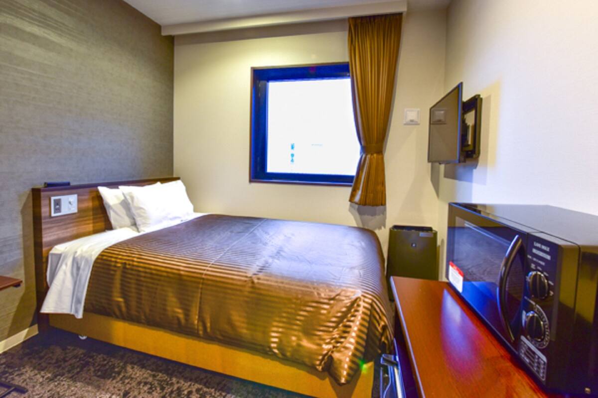 A hotel room with a large bed, a desk with a computer, a microwave, and a window with curtains.