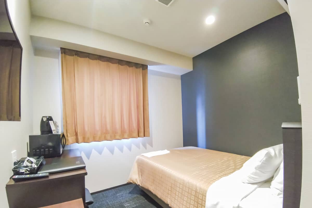 Een hotelkamer met een bed, een bureau met een computer en een raam met gordijnen.