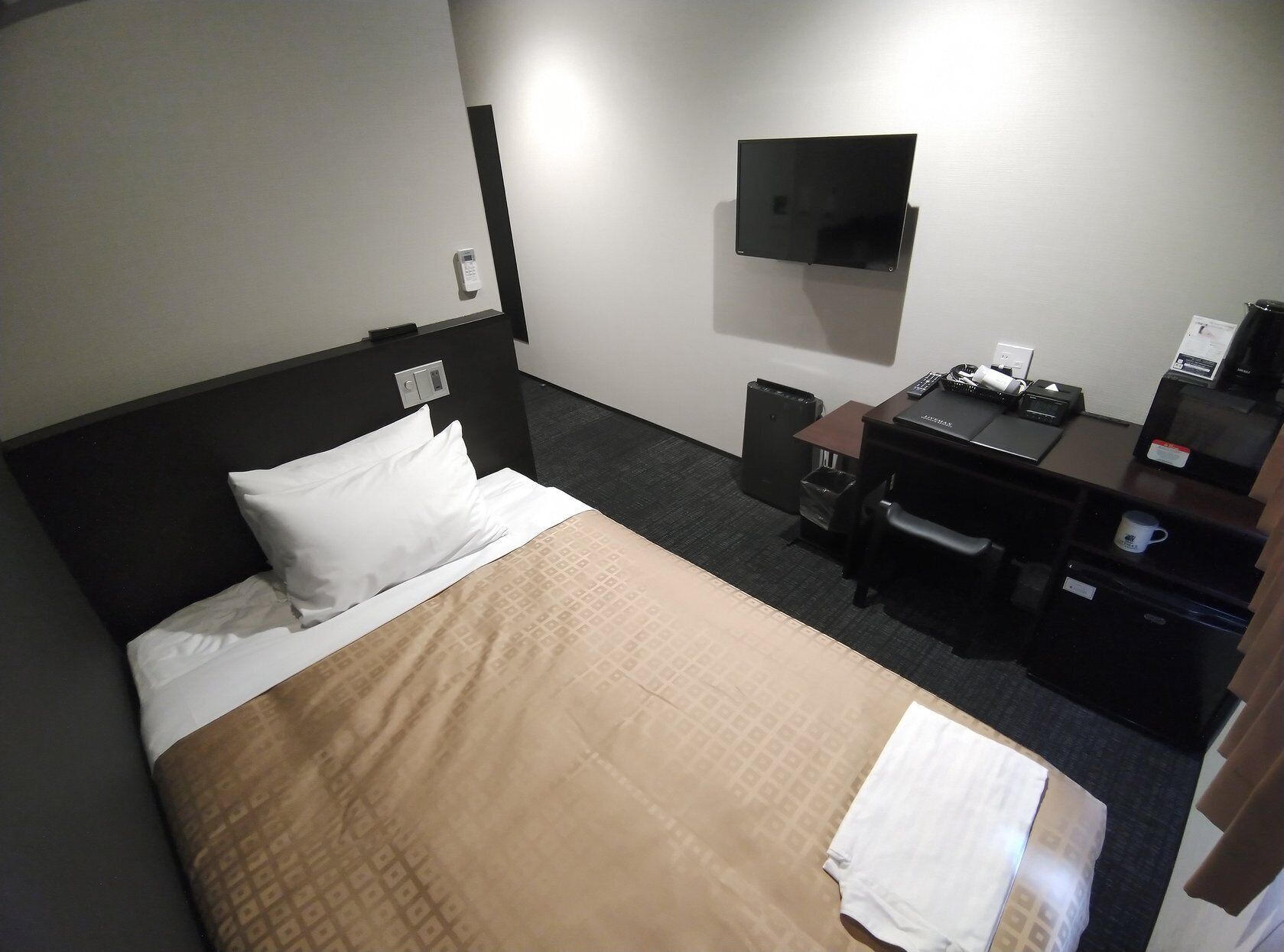 A hotel room with a bed, a desk, a television, and a trash bin.