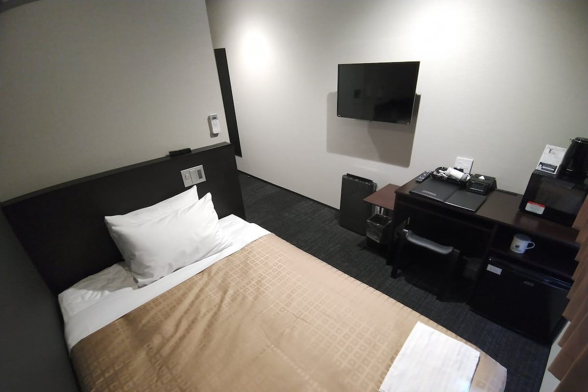 Een hotelkamer met een bed, een bureau, een televisie en een prullenbak.