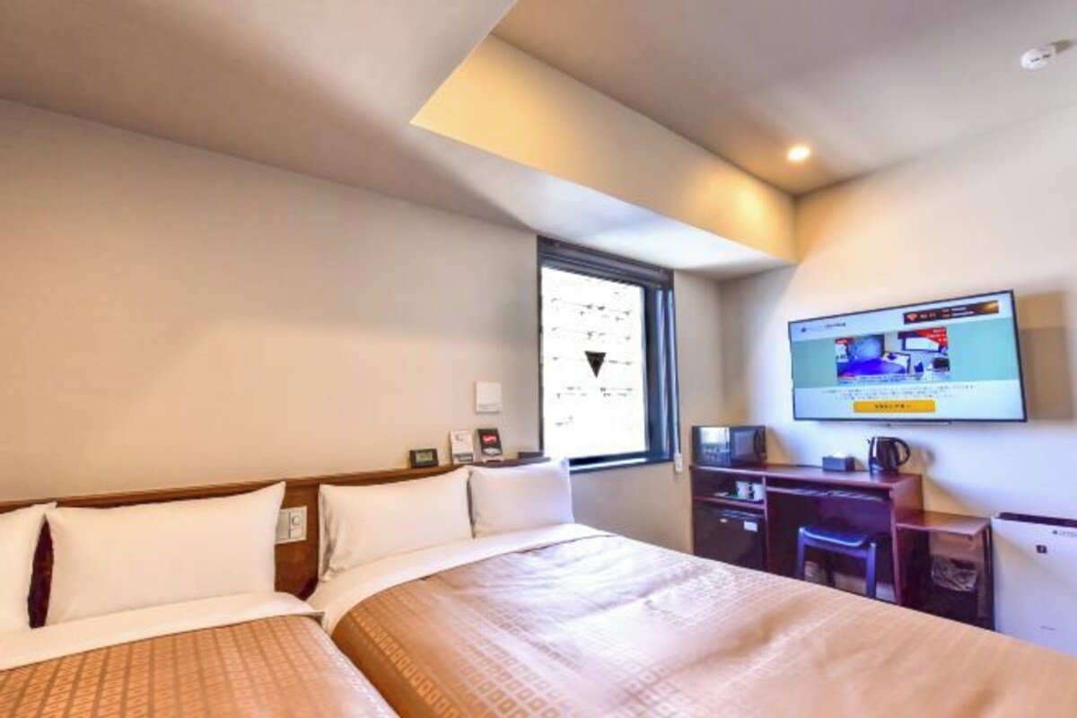 Ein Hotelzimmer mit einem großen Bett, einem Schreibtisch und einem an der Wand befestigten Fernseher.