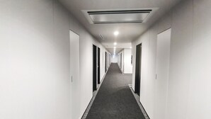 A long, narrow hallway with white walls and a carpeted floor, leading to multiple doors. - Hotel Livemax Kokura-ekimae (Kitakyushu)