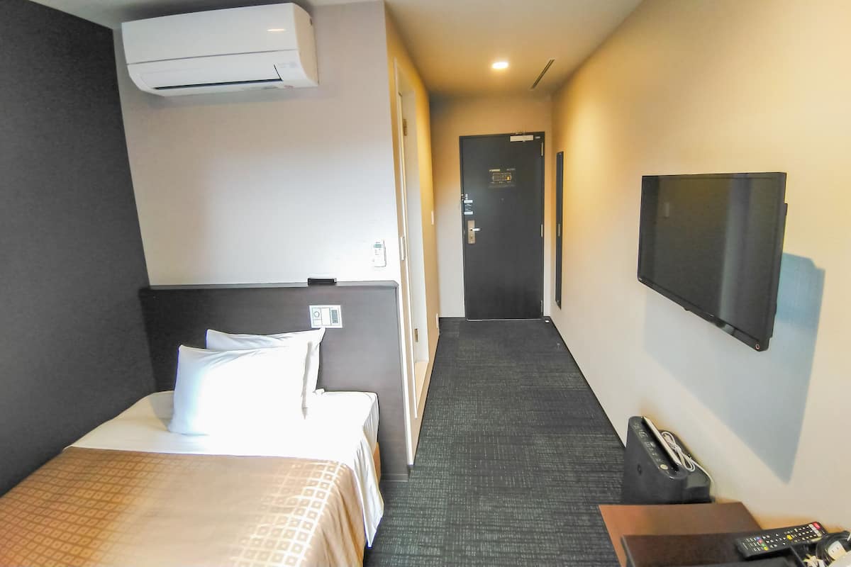 Hotelkamer met een bed, een televisie, een bureau, een stoel, een telefoon en een wandairconditioner.