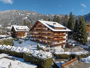 A multi-story wooden building with balconies, surrounded by snow-covered trees and mountains.