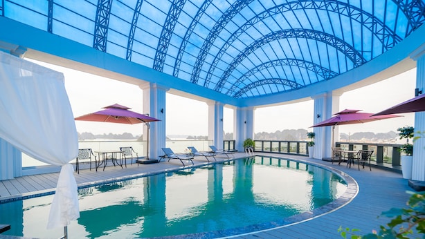 Una piscina interior con techo de cristal, sillas de descanso y sombrillas.