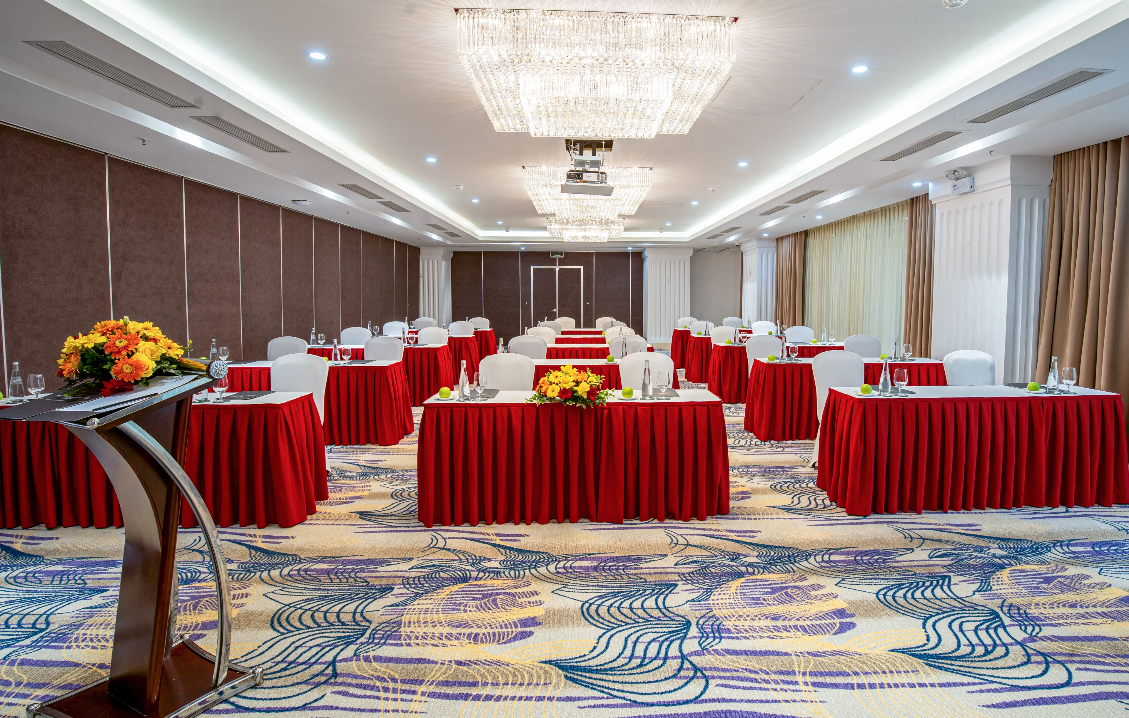 A conference room with red tables, white chairs, and a large chandelier.
